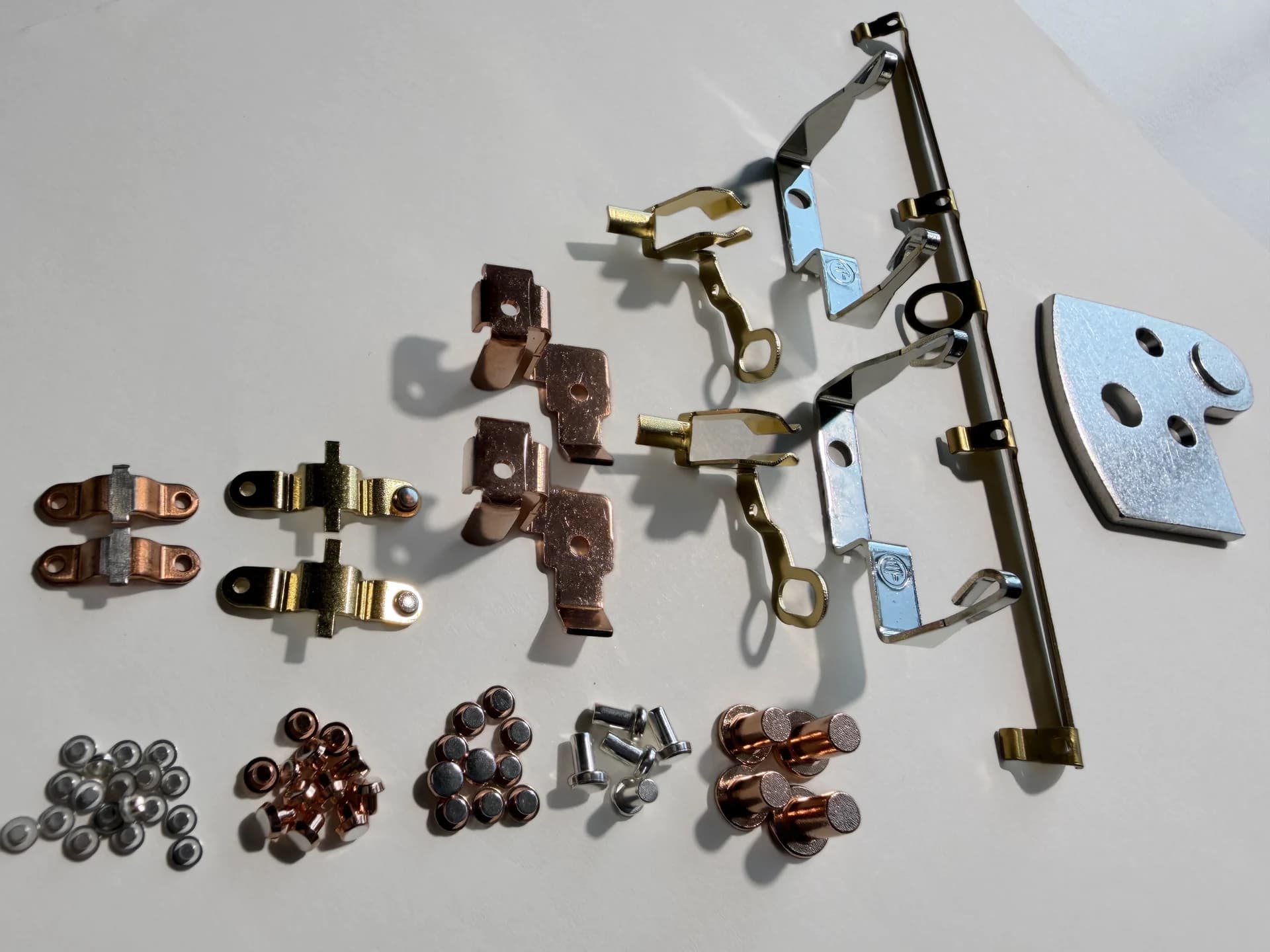 A photographed selection of custom electrical contact rivets and contact assemblies arranged on a light work surface.
